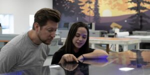 Two individuals focused on a digital printer in a professional office setting, engaged in a collaborative task.