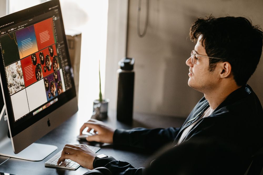 A man sitting at a desk with a computer screen, working on a trifold brochure layout.