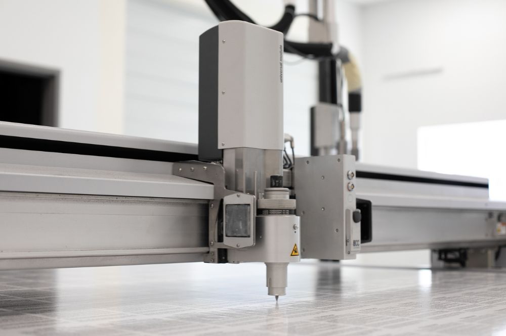 A machine is precisely cutting out vinyl on a large industrial printer.